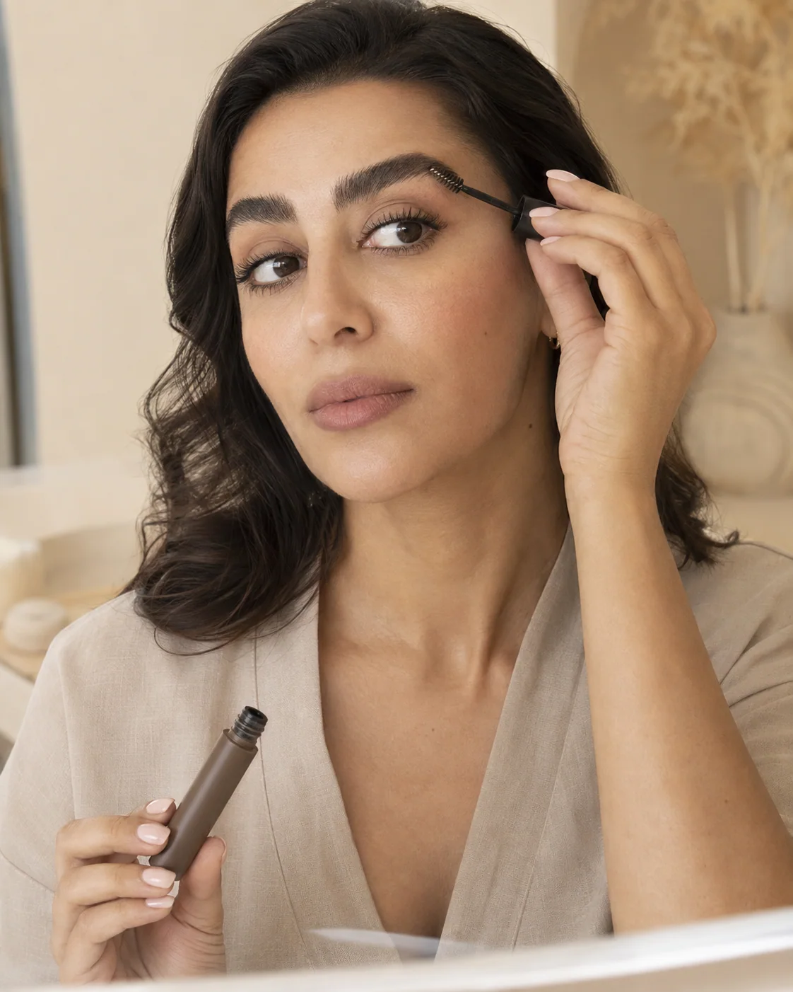 Woman brushing tinted brow gel through one eyebrow with a small spoolie wand